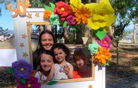 quatro criança posam numa moldura branca decorada com flores e a frase 
