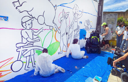 Cerca de uma dezena de pessoas junto de uma parede exterior parcialmente desenhada e pintada.