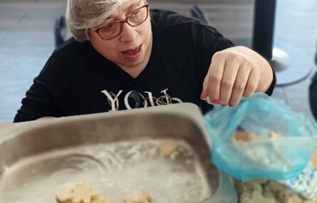 Uma pessoa mexe em massa e biscoitos preparados (ou ainda em fase de preparação).