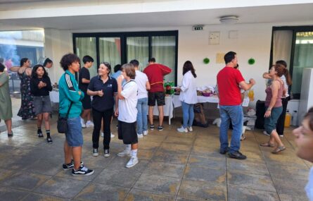 Imagem de espaço exterior com mais de uma dezena de pessoas a conversar – enquanto outras estão junto de mesas com bebidas e produtos alimentares.