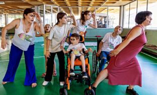 Sete pessoas, de várias idades, em espaço interior. Parecem estar a simular um gesto ou, possivelmente, a dançar.