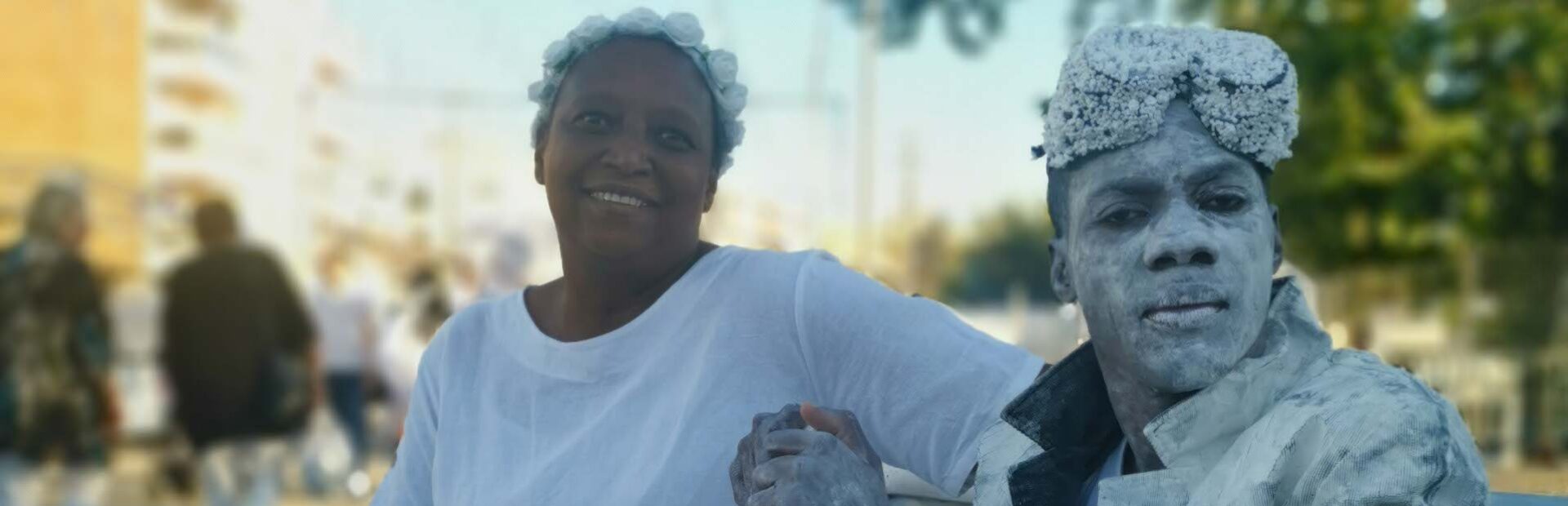Duas pessoas, ambas vestidas de branco, sentadas num banco colocado numa rua.