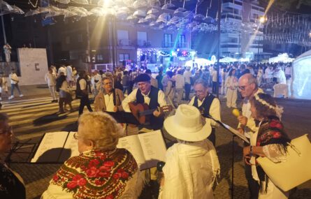 Vários elementos de grupo musical em atuação na rua. Ao fundo da imagem imensas pessoas e ornamentação relativa à Noite Branca.