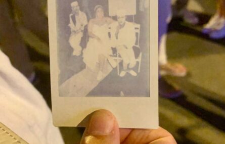 Uma pessoa segura, na mão, uma fotografia tipo “Polaroid”. A imagem na fotografia ainda está em fase de impressão.