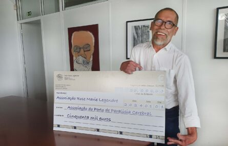 Uma pessoa sorridente segura um cheque em tamanho gigante. O referido cheque indica ser um donativo de 50 mil euros da Associação Rose Marie Legendre à Associação do Porto de Paralisia Cerebral.