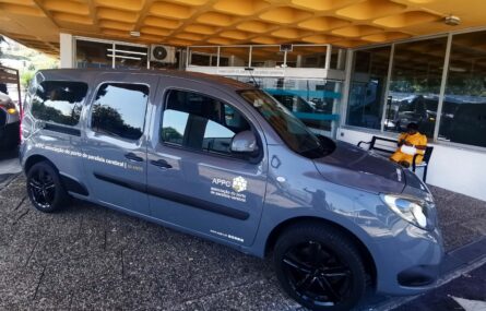 Viatura, de cor cinzento escuro, estacionada junto da entrada principal do Centro de Reabilitação da APPC. Ao fundo surge uma pessoa sentada em banco exterior.