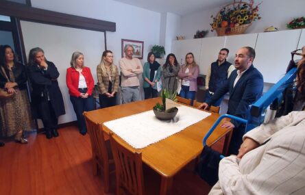 Grupo de pessoas em apartamento interior – no que aparenta ser a zona de cozinha e convívio. Ao centro de imagem uma mesa com quatro cadeiras.