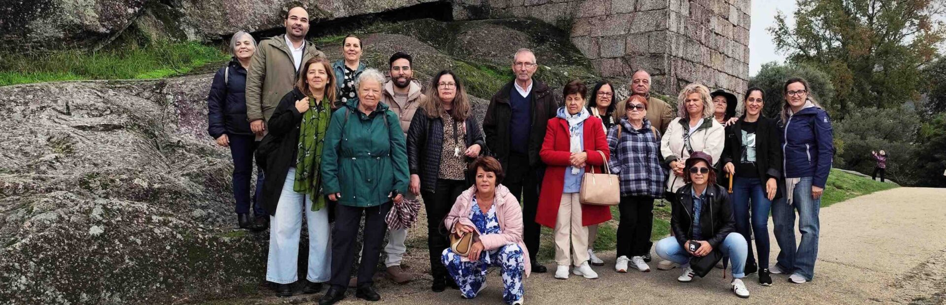 Várias pessoas em passadiço de metal no que aparenta ser zona de muralhas de um castelo. Em primeiro plano, de costas, uma pessoa usa o telemóvel para fotografar as restantes.