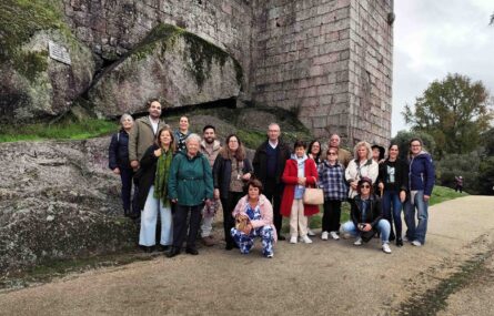 Várias pessoas em passadiço de metal no que aparenta ser zona de muralhas de um castelo. Em primeiro plano, de costas, uma pessoa usa o telemóvel para fotografar as restantes.