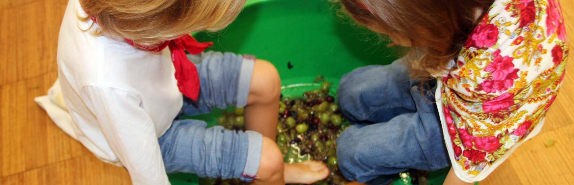 Duas crianças pisam uvas em bacia de plástico.