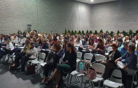 Fotografia de espaço interior amplo. Mais de uma centena de cadeiras com pessoas sentadas.