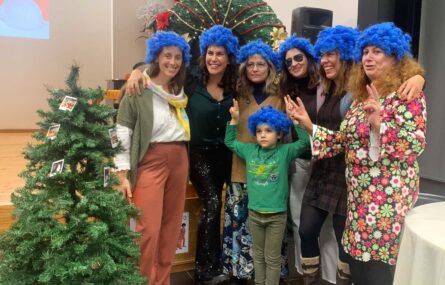 Seis adultos e uma criança (todos com cabeleiras azuis). Junto do grupo uma árvore de Natal com algumas fotografias penduradas.