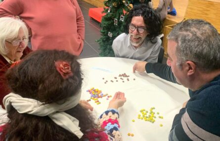 Cinco pessoas junto de uma mesa com imensas drageias coloridas (de chocolate). Aparentam organizar as drageias por cores.