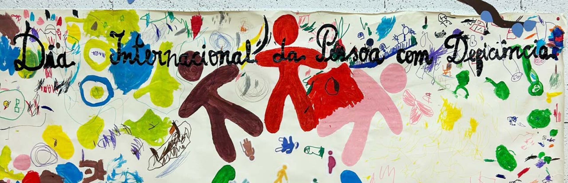 Cartaz colorido afixado numa parede. Vários desenhos e a frase: Dia Internacional da Pessoa com Deficiência.