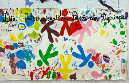 Cartaz colorido afixado numa parede. Vários desenhos e a frase: Dia Internacional da Pessoa com Deficiência.