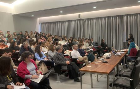 Imagem de auditório interior com várias dezenas de pessoas sentadas na zona da plateia. À direita da imagem, junto de uma mesa, estão duas pessoas sentadas. Uma outra pessoa, junto de um púlpito, aparenta estar a falar.