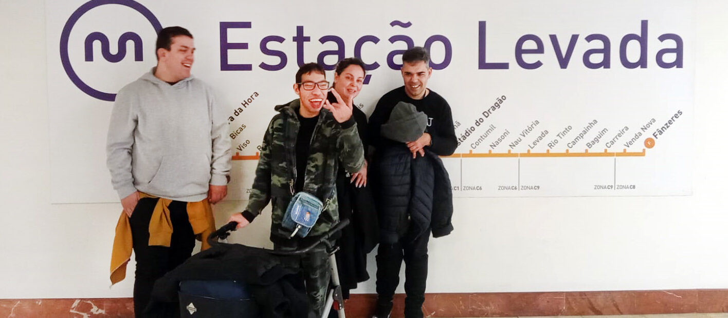 Grupo de quatro pessoas, sorridentes, junto de uma parede. Na referida parede surge a simbologia da empresa Metro do Porto, a identificação da estação na qual se encontravam (Estação da Levada) e, ainda, um mapa das restantes estações da linha de metro utilizada.