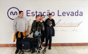 Grupo de quatro pessoas, sorridentes, junto de uma parede. Na referida parede surge a simbologia da empresa Metro do Porto, a identificação da estação na qual se encontravam (Estação da Levada) e, ainda, um mapa das restantes estações da linha de metro utilizada.