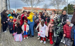 Grupo de várias dezenas de crianças e adultos em passeio por zona exterior. As crianças estão mascaradas. Os rostos identificáveis das crianças foram digitalmente desfocados.