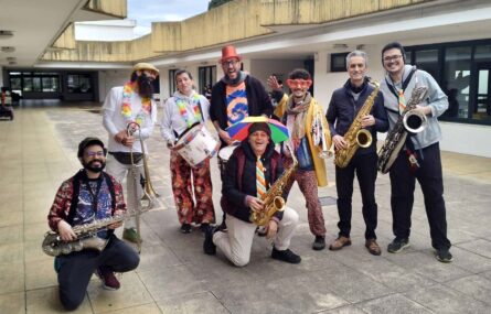 Grupo de oito adultos, alguns mascarados, em espaço exterior da Villa Urbana de Valbom. Todos os adultos seguram um instrumento musical.