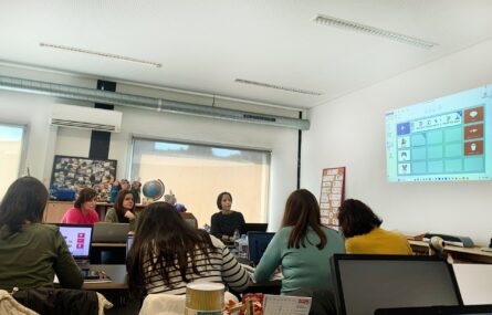 Fotografia de sala de formação com diversas mesas, cadeiras e material informático. Na imagem surgem 11 pessoas e vê-se uma projeção multimédia na parede.