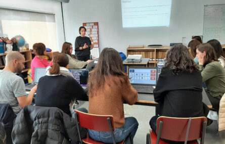 Fotografia de sala de formação com diversas mesas, cadeiras e material informático. Na imagem surgem 11 pessoas e vê-se uma projeção multimédia na parede.