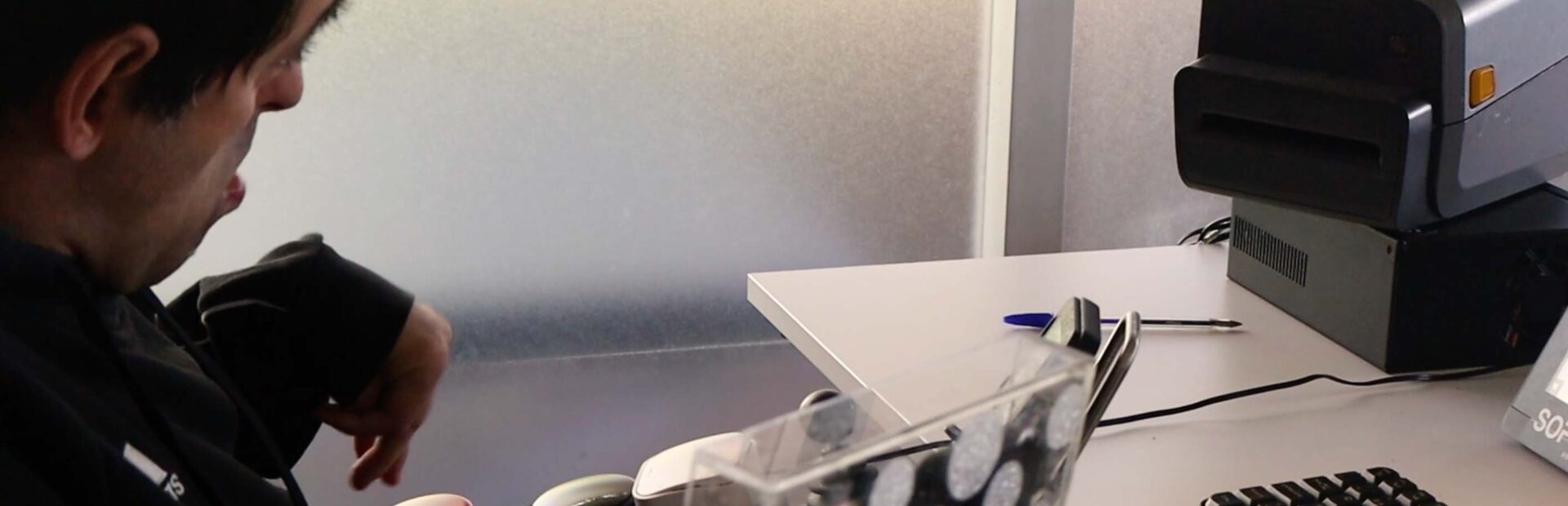 Uma pessoa em frente a computador e impressora parece selecionar algo com recuso a botões instalados em braço de cadeira.
