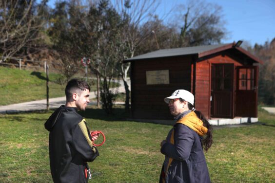 Duas pessoas sorriem e conversam em ambiente exterior ajardinado.
