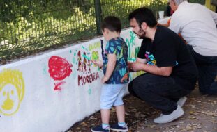 Duas crianças e dois adultos pintam uma parede com desenhos e palavras