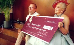 Duas pessoas sentadas em degraus de escadas. Nas mãos seguram um cheque em tamanho gigante.
