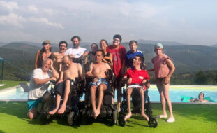 Grupo de doze pessoas em espaço relvado junto de uma piscina. Na piscina surge uma pessoa relaxada em cima de um colchão de ar.