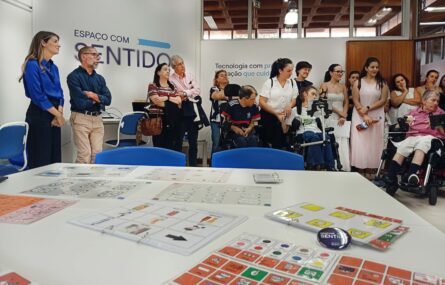 Mais de uma dezena de pessoas em sala apetrechada com diverso equipamento informático. Em primeiro plano uma mesa com diversas tabelas de comunicação pousadas. Numa das paredes, com letras grandes, surge a frase “Espaço com Sentido”.