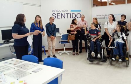 Cerca de uma dezena de pessoas, maioritariamente sorridentes, em sala apetrechada com diverso equipamento informático. Em primeiro plano uma mesa com diversas tabelas de comunicação pousadas. Numa das paredes, com letras grandes, surge a frase “Espaço com Sentido”.