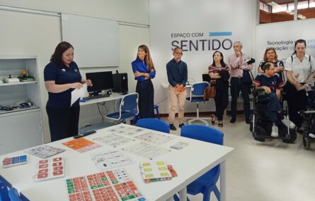 Oito pessoas em sala apetrechada com diverso equipamento informático (em mesas e prateleiras). Em primeiro plano uma mesa com diversas tabelas de comunicação pousadas. Numa das paredes, com letras grandes, surge a frase “Espaço com Sentido”.