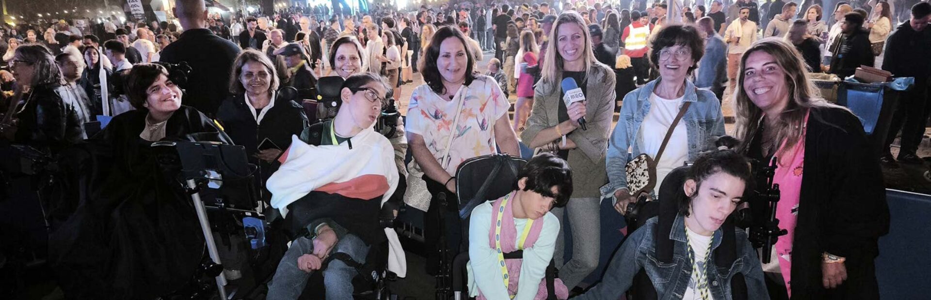 Grupo de uma dezena de pessoas fotografadas em ambiente noturno com várias centenas de pessoas igualmente visíveis na imagem. Ao centro da imagem uma das pessoas segura um microfone identificado com a expressão “Fundação MEO”.