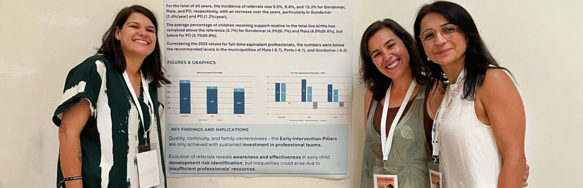 Três pessoas, sorridentes, junto de um poster com informações (afixado numa parede).