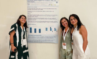 Três pessoas, sorridentes, junto de um poster com informações (afixado numa parede).